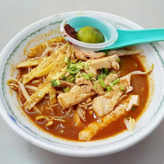 Semangkuk Laksa Sarawak pekat berwarna kemerahan dengan bihun, udang, telur dan ayam.